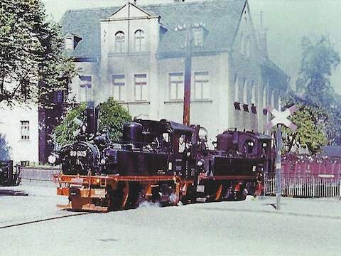 Die Aufnahme zeigt die Lokomotiven 99 605 und 99 573 mit einem GmP im Sommer 1954 beim Überqueren der Bahnhofsstraße zwischen Kirch­berg und Kirchberg Hp.