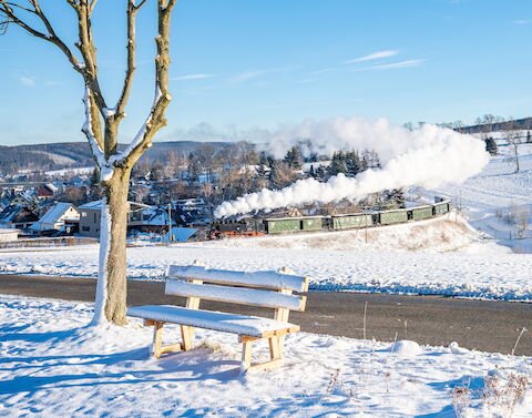 Die „Fotokurve“ am Hofweg in Cranzahl mit dem Bärenstein im Hintergrund hielt Hendrik Flath am 25. Dezember 2024 im Bild fest. An diesem ersten Weihnachtsfeiertag führte 99 1785-7 den Zug nach Oberwiesenthal.